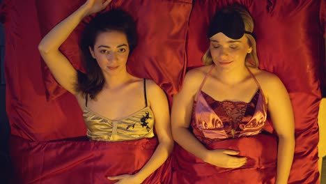 Flirty-girls-lying-on-silk-bed-linen,-seductively-looking-at-camera,-temptation