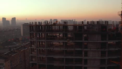 Aerial-Shot-of-the-Building-in-the-Process-of-Construction.-Labor-working-in-big-construction-site.-In-the-Background-Working-Crane-and-city