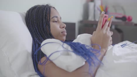 Porträt-von-afroamerikanischen-Mädchen-mit-Dreadlocks-liegen-im-weißen-Bett-und-mit-Smartphone.-Junge-Frau-surfen-Internet-in-der-Nacht.-Social-Media-Sucht,-Lebensstil.