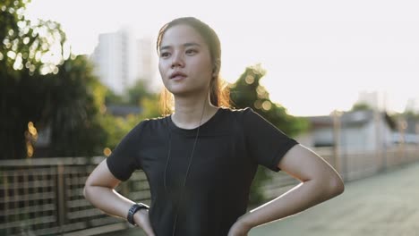 Attractive-caucasian-woman-athlete-running-resting-exhausted-after-a-cardio-workout-exercise-in-the-urban-city-sunset.-Jogging-lifestyle-healthy.-Girl-runner-wearing-earphones-listening-to-music.