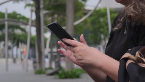 Manos-de-mujer-usando-el-teléfono-inteligente-en-una-moderna-calle-turística-de-la-ciudad