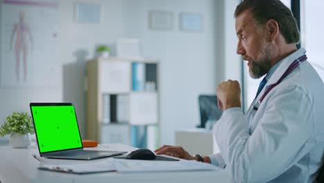 Family-Medical-Doctor-está-haciendo-una-videollamada-con-el-paciente-en-una-computadora-con-pantalla-verde-en-una-clínica-de-salud.-Assistant-in-Lab-Coat-está-hablando-sobre-problemas-de-salud-en-la-oficina-del-hospital.