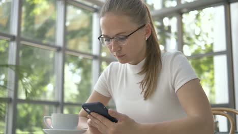 Frau-mit-Brille-surft-Internet-mit-Handy-im-Café