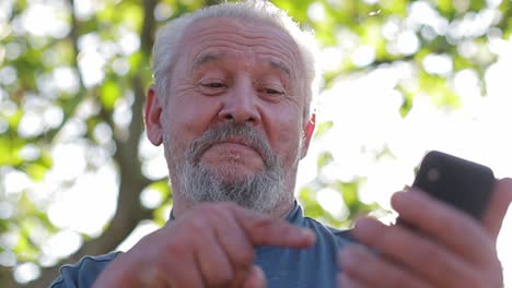 Viejo-hombre-de-pelo-gris-con-barba-utiliza-un-teléfono-inteligente-moderno