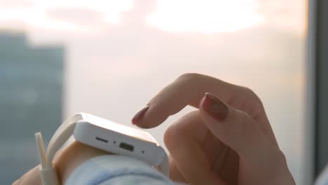 Vista-lateral-de-cerca---mano-de-mujer-usando-el-reloj-inteligente-blanco-ponible-en-la-oficina