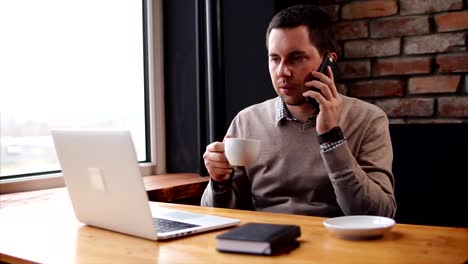 El-hombre-habla-por-teléfono-y-mirando-el-portátil-durante-las-vacaciones-en-el-café