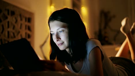 Close-up-of-young-attractive-woman-using-tablet-computer-at-night-time-lying-in-bed-at-home