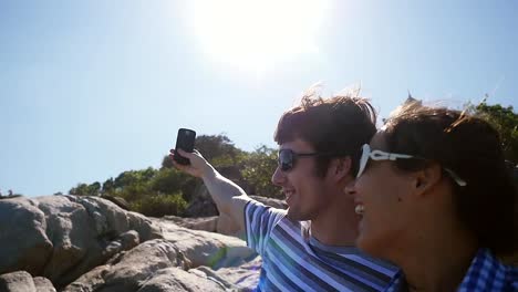 Young-smiling-couple-wearing-sunglasses-taking-selfie-portrait-by-beautiful-mountain-with-lense-flare-effects-on-the-sun-on-the-background-in-slow-motion.-1920x1080