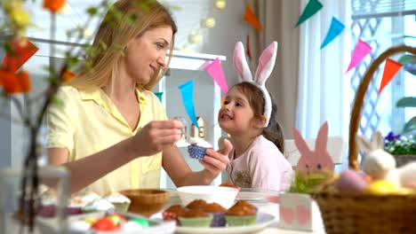 Joven-madre-y-su-pequeña-hija-con-orejas-de-conejo-divertidos-cocinar-cupcakes-de-Pascua