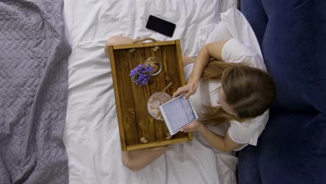 Top-view-woman-eating-breakfast-and-using-touchpad