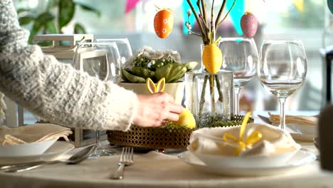 Young-woman-setting-easter-festive-table-with-bunny-and-eggs-decoration