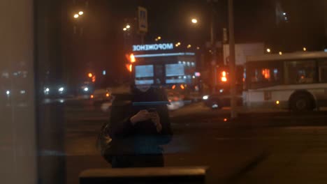 Woman-with-cell-at-bus-stop-in-night-city