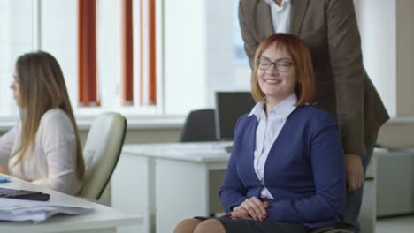 Man-Helping-Disabled-Female-Colleague-with-Riding-Wheelchair-in-Office