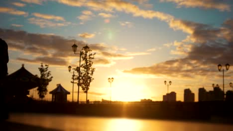 Caring-man-with-a-disabled-woman-in-wheelchair-walking-through-the-quay-at-sunset