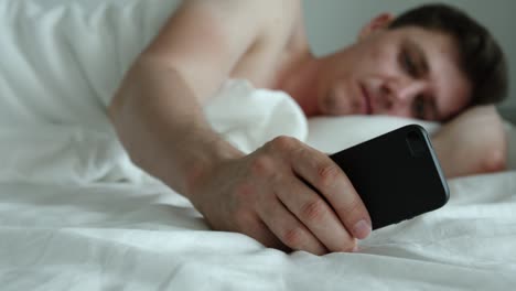 Young-adult-man-lies-on-a-bed-and-uses-phone---feet-level