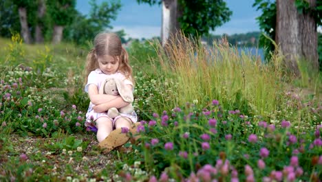 Una-niña-jugando-con-un-conejo-de-juguete-en-el-Prado-entre-el-trébol-de-flores