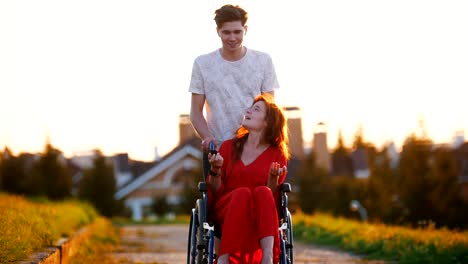 Smiling-Young-Man-Rolls-A-Red-Haired-Girl-On-A-Wheelchair,-Who-Tells-Him-Something