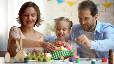 Beautiful-family-putting-dyed-Easter-eggs-into-basket,-Christians-traditions