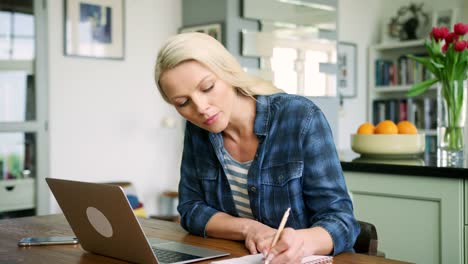 Attraktive-blonde-Frau-auf-Laptop-tippen-und-Schreiben-von-Notizen