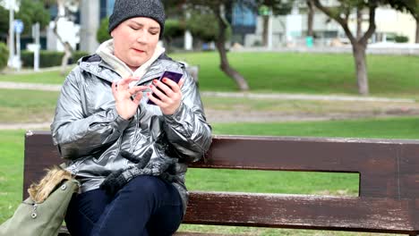 Frau-sitzt-auf-einer-Parkbank-mit-smartphone