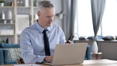 Empresario-de-pelo-gris-con-Smartphone-en-el-lugar-de-trabajo