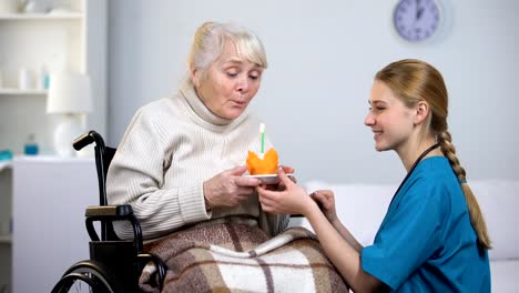 Doctor-dando-pastel-de-cumpleaños-a-la-mujer-con-discapacidad,-señora-de-soplar-la-vela