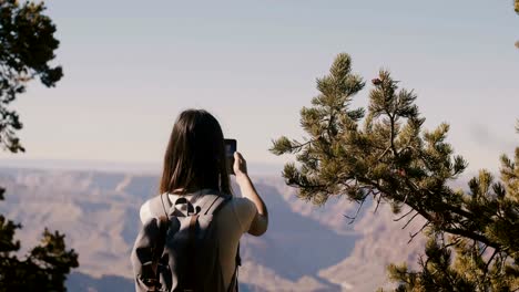 Rückblick-auf-die-glückliche-junge-Touristin,-die-Smartphone-fotografiert-und-die-epische-Bergkulisse-des-Grand-Canyon-in-Arizona-USA-zeigt.