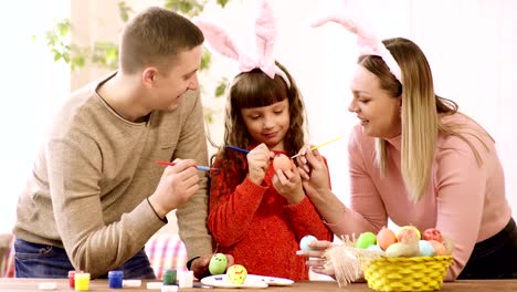 mamá-y-su-hija-en-las-orejas-de-conejo-y-papá-decoran-los-huevos-para-las-vacaciones-de-Pascua.