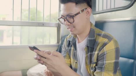 Traveler-Asian-man-using-smartphone-checking-social-media-while-taking-a-train.