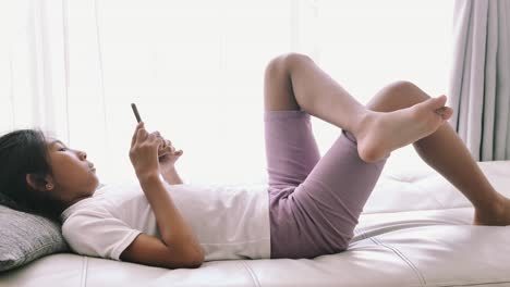 Mädchen-mit-Smartphone-auf-Sofa-zu-Hause