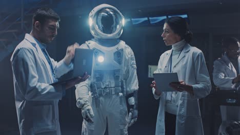 Diverse-Team-of-Aerospace-Scientists-and-Engineers-Wearing-White-Coats-have-Discussion,-Use-Computers,-Design-New-Space-Suit-Adapted-for-Galaxy-Exploration-and-Travel.-Constructing-Astronaut-Suit