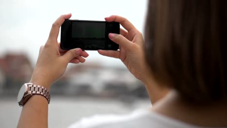 Close-Up-hands-asian-woman-using-smartphone-take-photo.-Sending-photo-social-media-beside-fence-at-river.