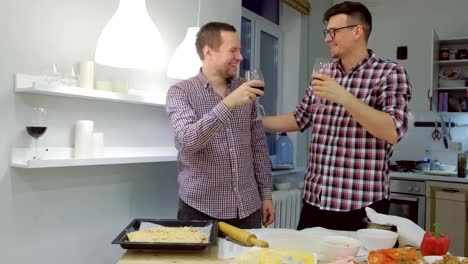 Men-gay-clink-glasses,-drink-wine-and-cook-pizza-in-the-kitchen.-Gay-family-life.