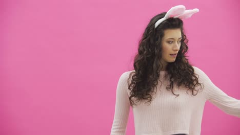 Beautiful-young-girl-standing-on-a-pink-background.-During-this,-there-are-ears-of-rabbits-on-the-head.-Performs-rabbits-rhythmic-movements-with-the-hands-of-a-call.