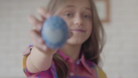 Cute-little-girl-holding-blue-easter-egg-with-painted-heart-in-hand