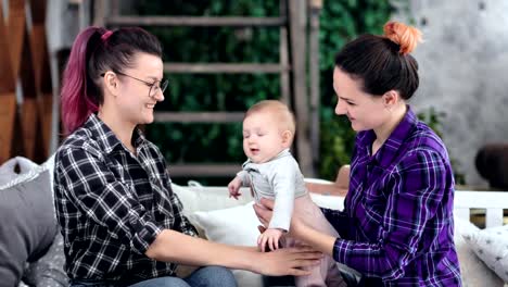 Two-happy-smiling-young-woman-playing-with-little-baby-kissing-and-feeling-love-having-good-time