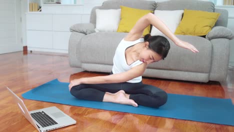 Asiatische-Yoga-Trainerin-mit-Laptop-für-Live-Unterricht,-wie-man-Yoga-im-Wohnzimmer-zu-Hause-zu-tun.-Junge-gesunde-weibliche-Bewegung-für-den-fitten-Körper.-Frauen-üben-zu-Hause-Konzept.