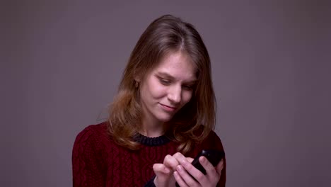 Young-female-student-swiping-photos-on-smartphone-and-emotionally-reacting-on-gray-background.