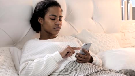 Junge-afrikanische-Frau-mit-Smartphone-beim-Entspannen-im-Bett