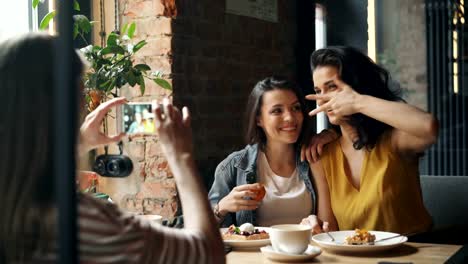 Atractivas-señoritas-tomando-fotos-en-café-posando-para-la-cámara-del-teléfono-inteligente