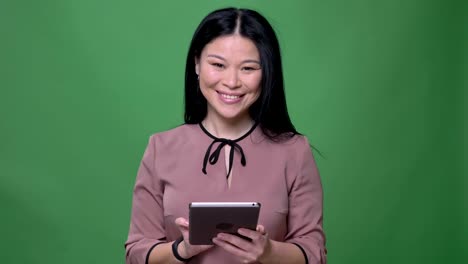 Nahaufnahme-von-jungen-attraktiven-asiatischen-Frau-mit-schwarzen-Haaren-SMS-auf-dem-Tablet-mit-Hintergrund-isoliert-auf-grün