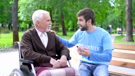 Positive-männliche-Freiwillige-unterhalten-behinderten-Patienten,-hören-gemeinsam-Musik