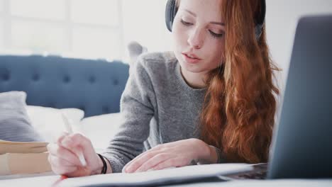 Estudiante-universitaria-femenina-acostada-en-la-cama-usando-auriculares-y-trabajando-en-la-computadora-portátil---rodada-a-cámara-lenta