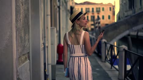 Attractive-caucasian-female-tourist-in-stylish-hat-searching-architect-building-during-walk-on-Venice