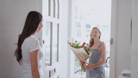 Frau-öffnet-Haustür-zu-Homosexuell-Partner-zu-Hause,-die-ihr-Bündel-von-Blumen-gibt