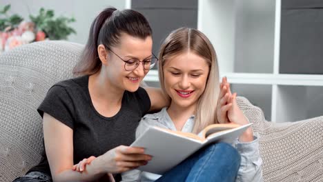 Two-smiling-homosexual-young-woman-reading-book-together-on-couch-feeling-love-and-tenderness