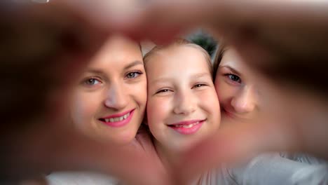 Close-up-face-happy-child-girl-showing-heart-gesture-by-hand-posing-two-lesbian-kissing-mother