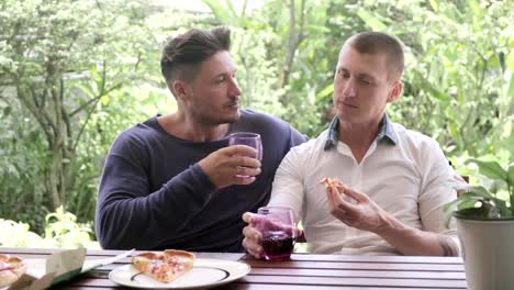 Gay-couple-having-pizza-for-lunch.-Holding-pizza-and-kisses.