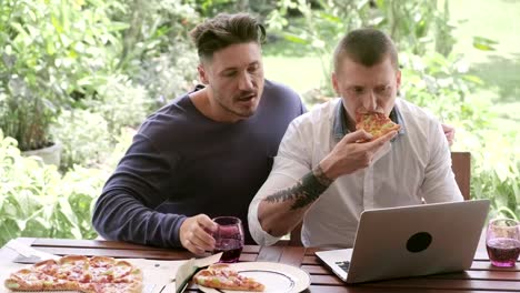 Gay-couple-having-pizza-for-lunch.-Browsing-and-eating-pizza.