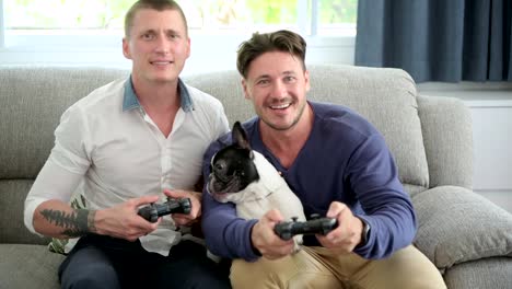 Pareja-gay-relajándose-en-el-sofá-con-el-perro-jugando-juegos.-Jugando.